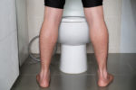 Man peeing to toilet bowl in restroom from back.