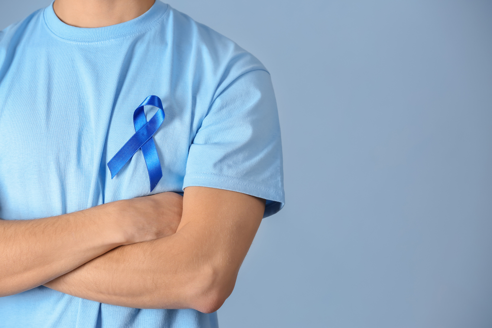 Young man wearing t-shirt with blue ribbon on color background.